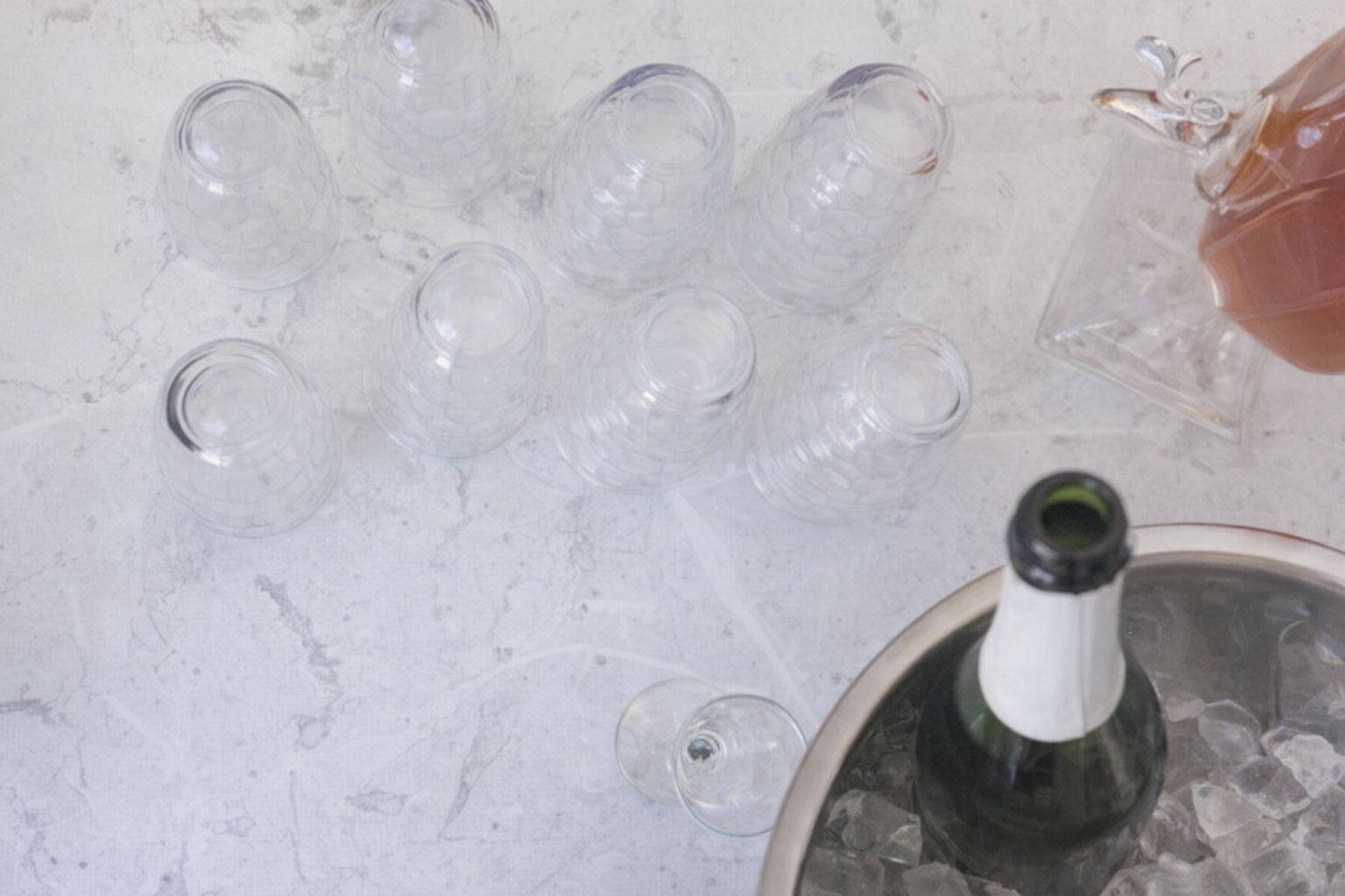 Glas, dryckeskanna och en flaska i iskylare på en ljus marmorskiva.